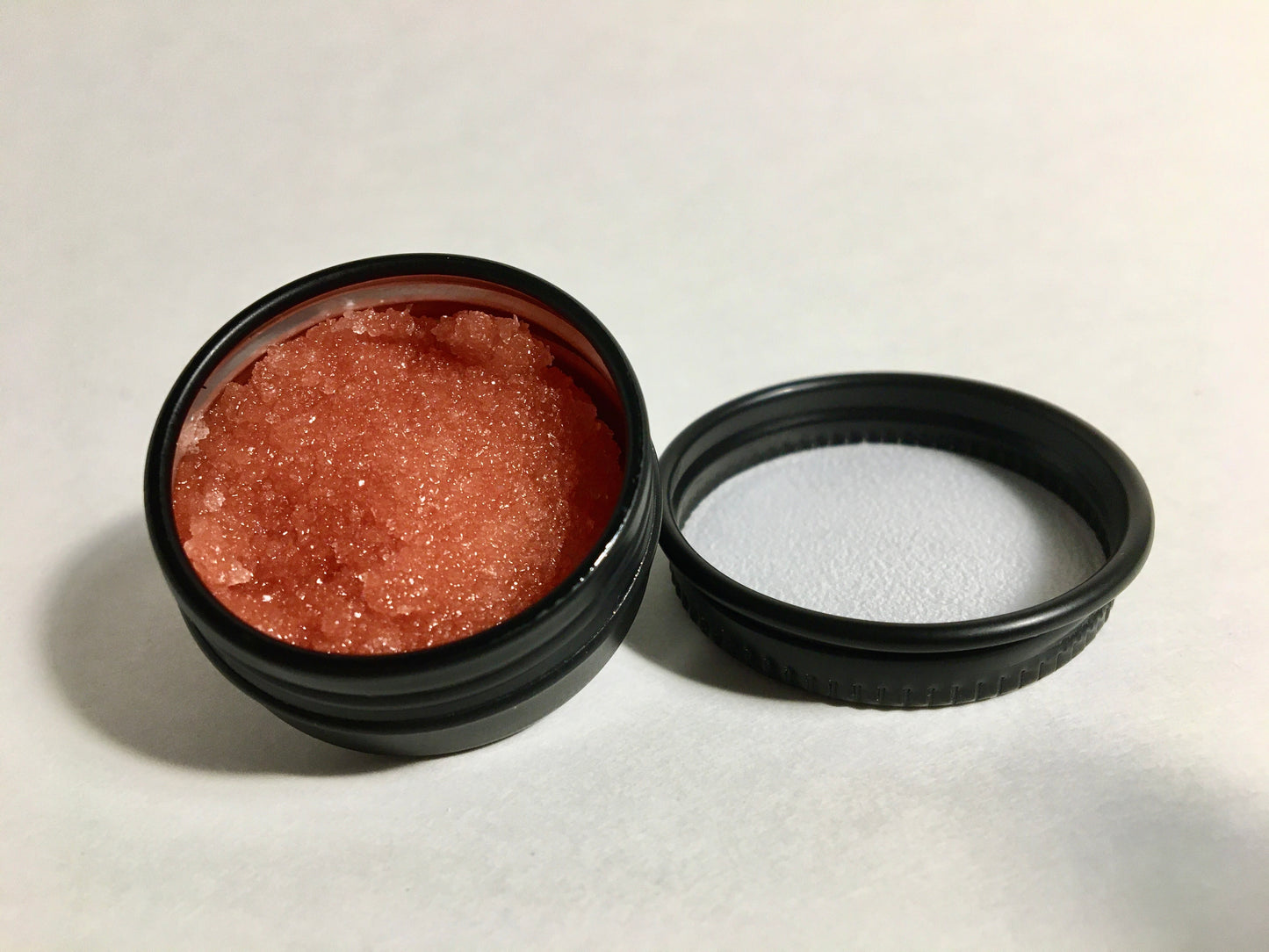 Exfoliant Sinfuly Sweet, focus sur la texture granulée et rouge sur arrière-plan blanc avec un différent angle de vue.